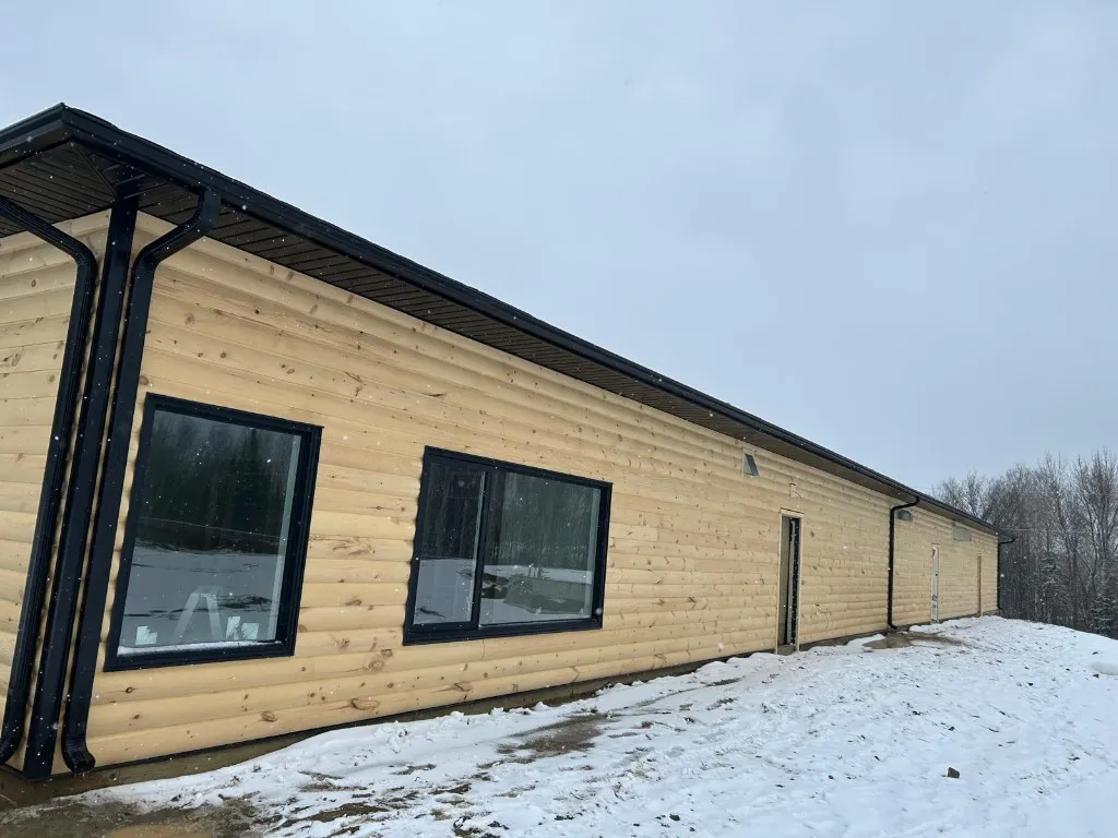 Long log-profile building photographed in winter with continuous black eavestrough, black soffit and fascia running the full roofline