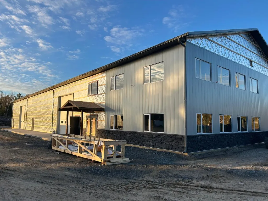 Large commercial steel building with white metal cladding and a stone-look base, eavestrough running along the low-slope roofline at sunset