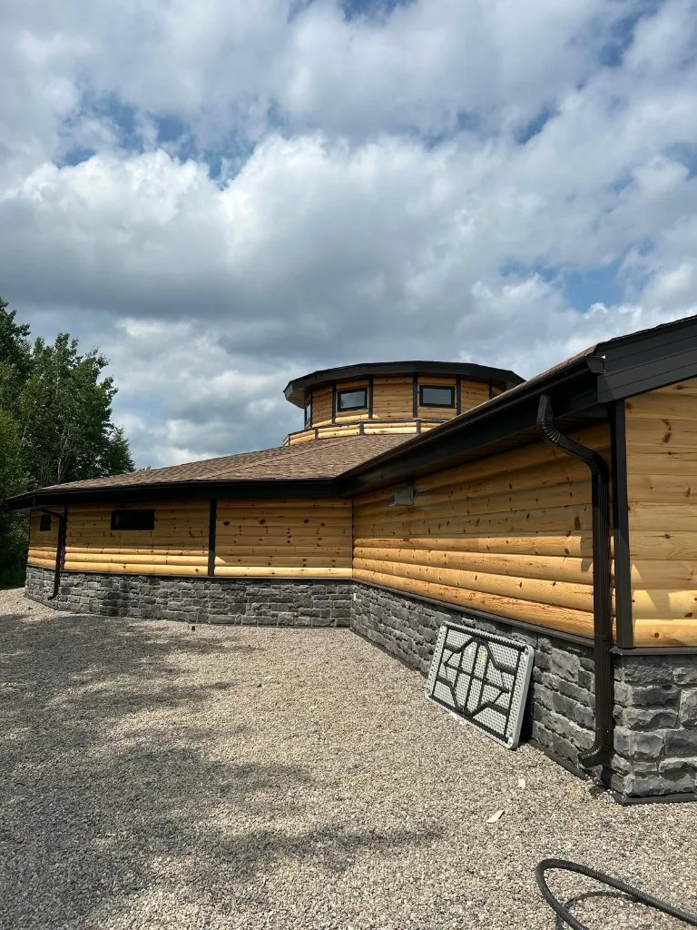 Log-profile home with an octagonal turret and stone skirt, brown eavestrough and a brown downspout with crimped elbows