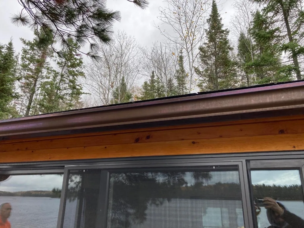 Copper eavestrough running along the pine soffit of a lakefront cabin, the sliding doors reflecting the Lake of the Woods shoreline